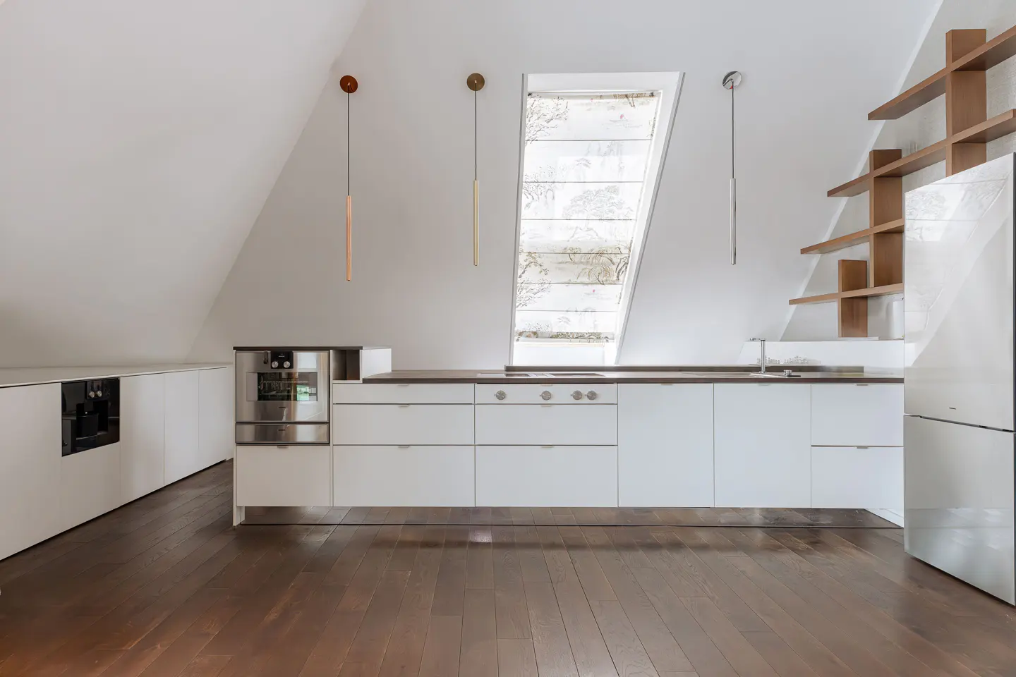 Attic kitchen with white cabinets, stainless steel appliances, and a wood floor. A window is above the counter, and wood shelves are on the right.