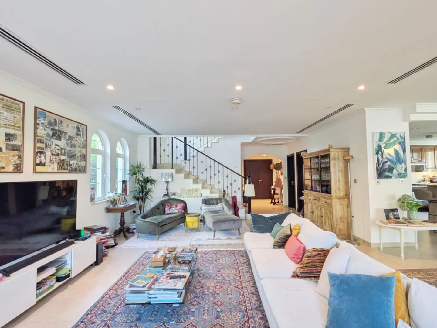 Bright living room with a white sofa, blue rug, and staircase. The walls are white, and there are large windows.