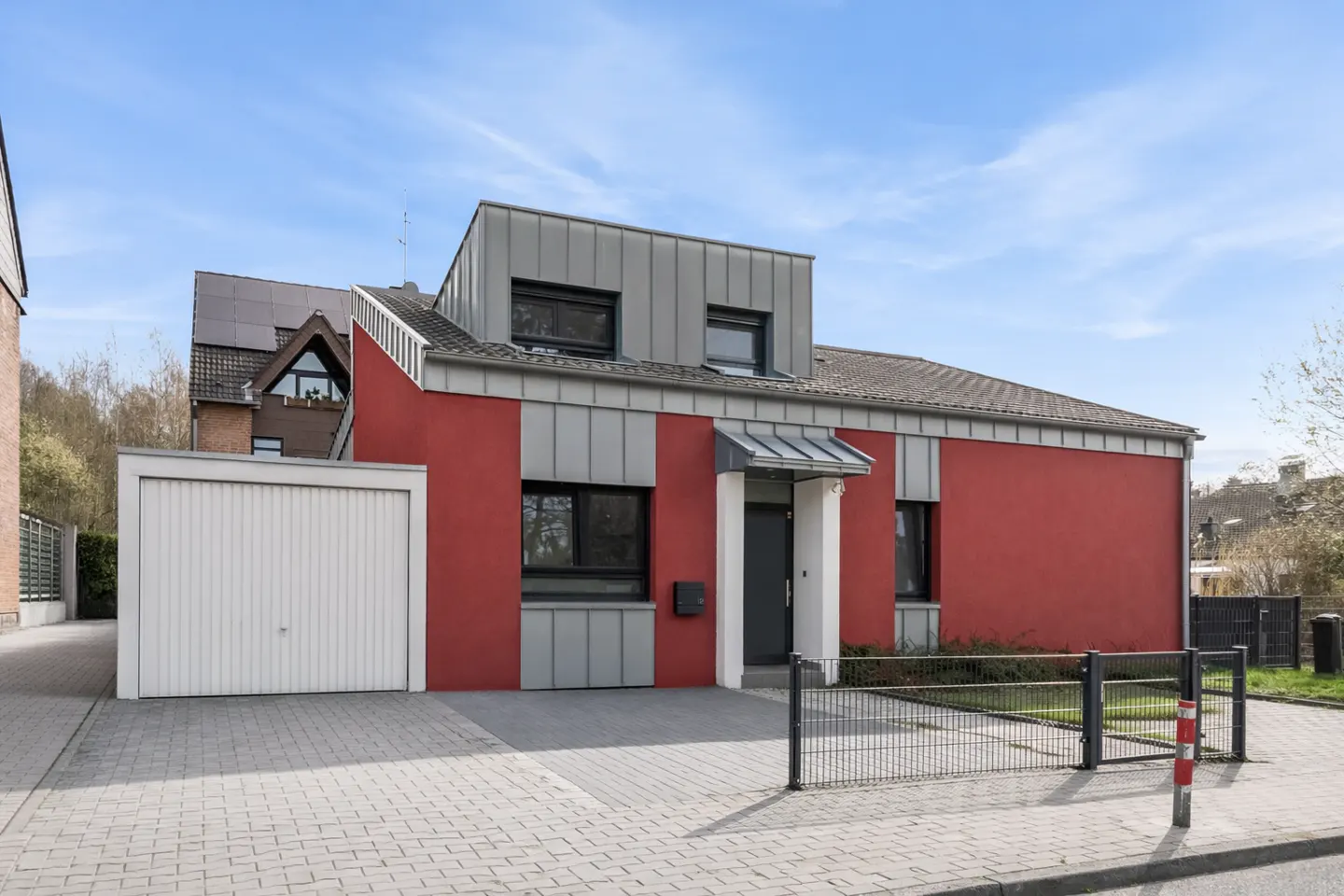A modern two-story house with red and gray siding, a gray roof, and a white garage under a blue sky.