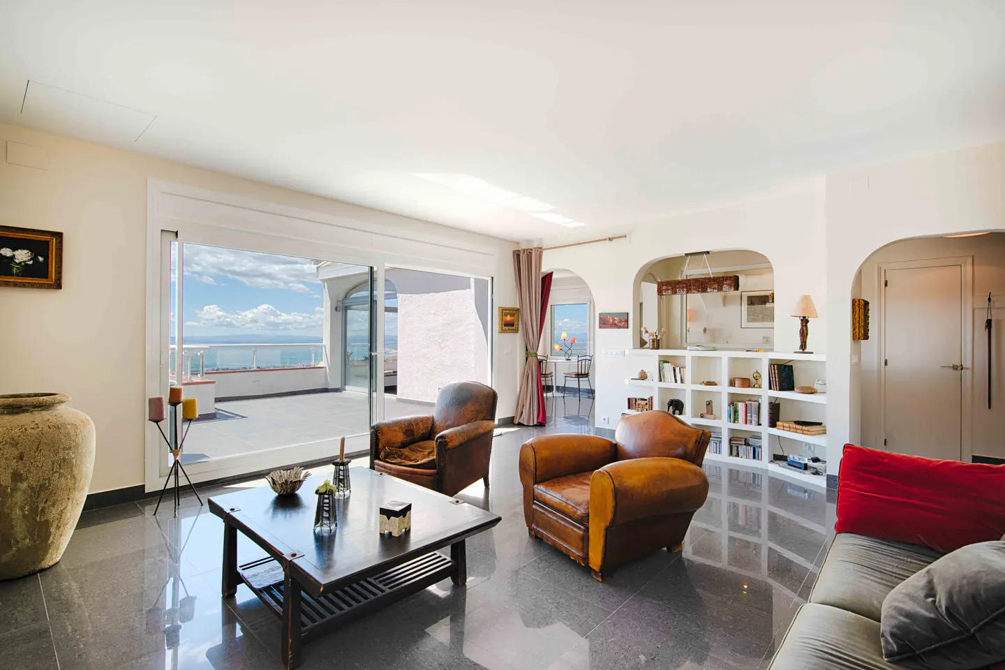 Bright living room with leather chairs, dark wood table, and ocean view from a large sliding glass door to a patio.