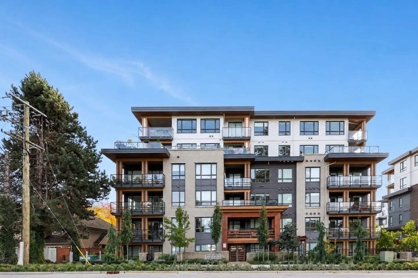 Modern apartment building with balconies, wood accents, and a blue sky background.