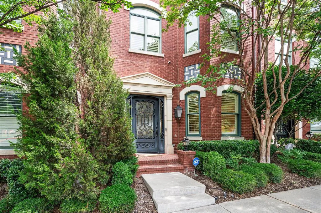 Red brick house with a decorative black door, green trim, and manicured landscaping.