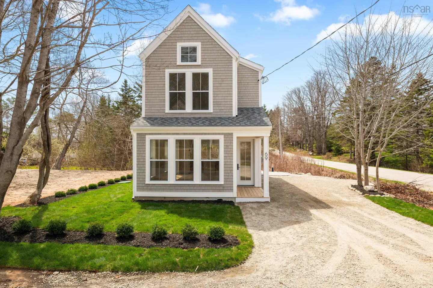Two-story gray house with white trim, green lawn, and gravel driveway on a sunny day.