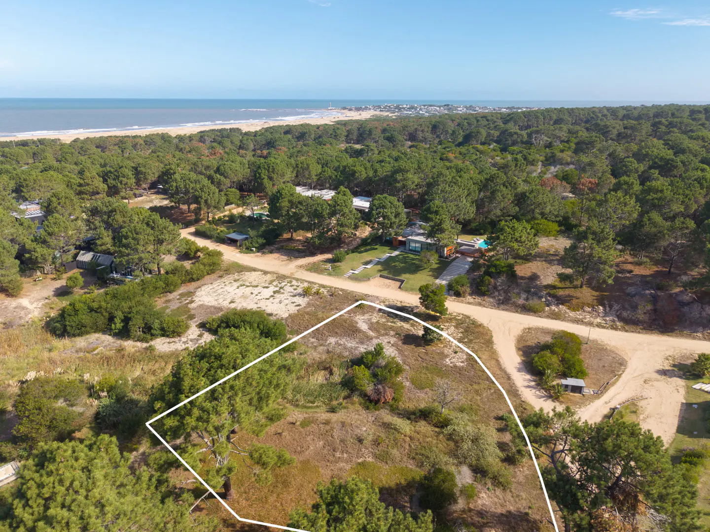 Aerial view of a vacant lot outlined in white, surrounded by trees, with the ocean and beach in the background.