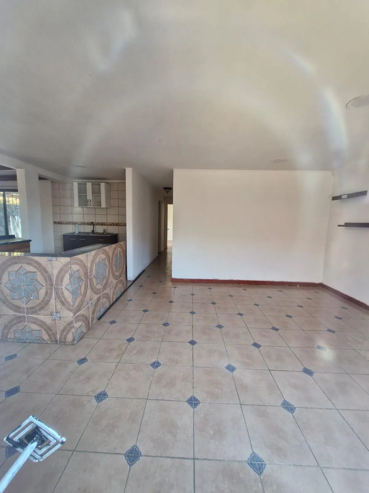 Open-concept living space with tile flooring, white walls, and a kitchen area with brown cabinets and a tiled backsplash.