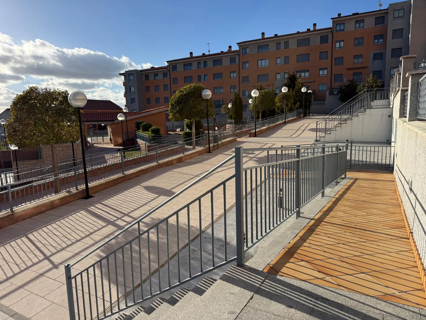 Exterior view of a modern apartment complex with walkways, stairs, and metal railings under a blue sky with clouds.