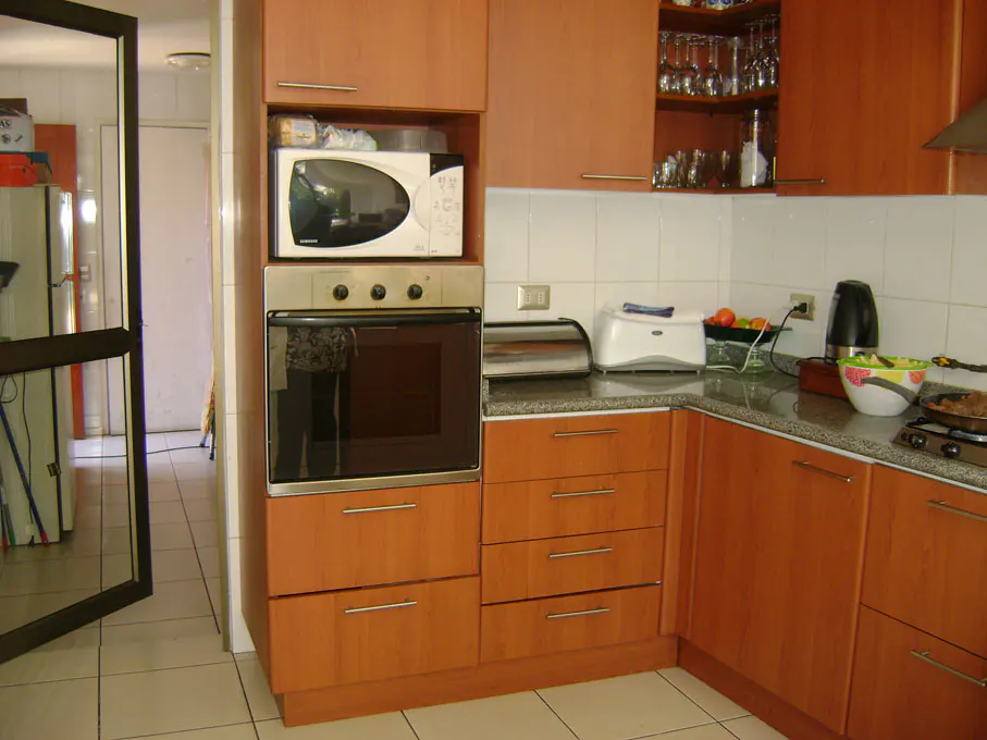 A kitchen with light brown cabinets, a microwave over an oven, and a door leading to another room.