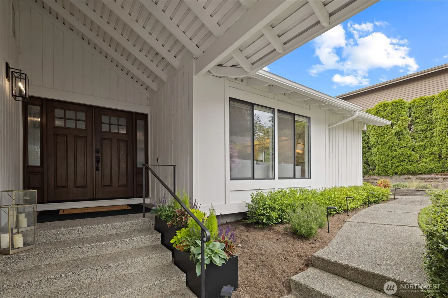 Exterior of a white house with a brown double door, concrete steps, and green landscaping.