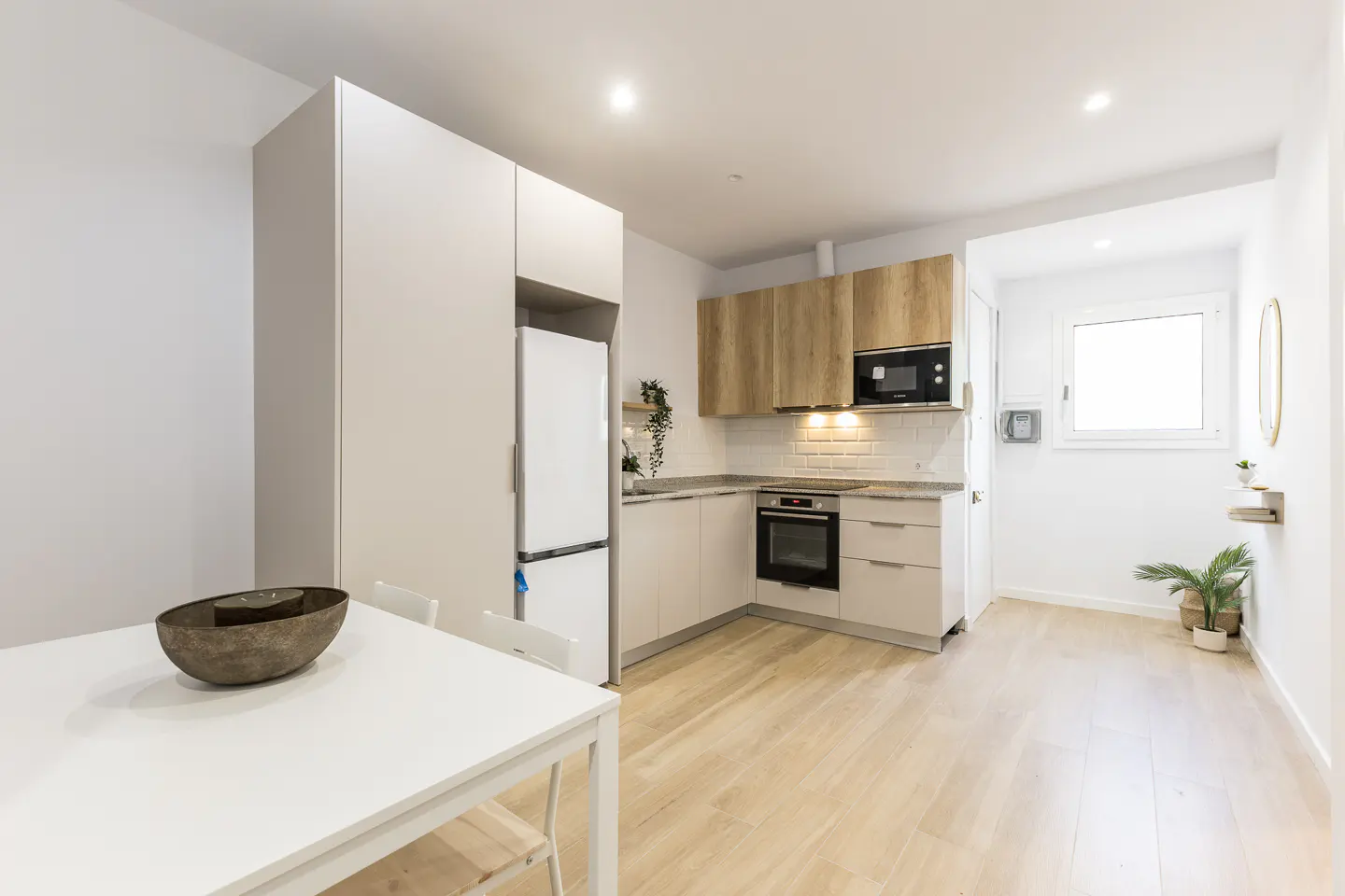 A bright, modern kitchen with white cabinets, wood accents, and a white dining table. A window provides natural light.