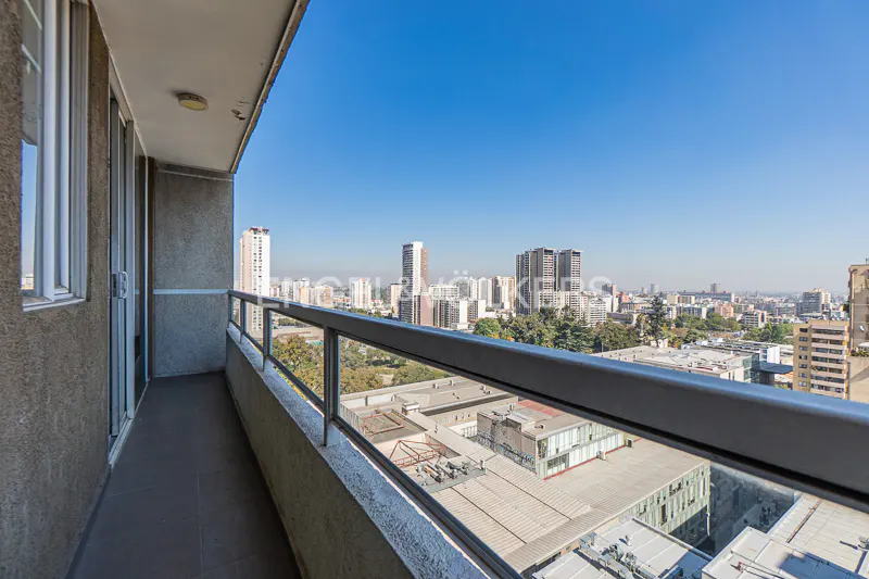Balcony view of a city skyline under a clear blue sky. Gray railings and a concrete balcony floor are visible.