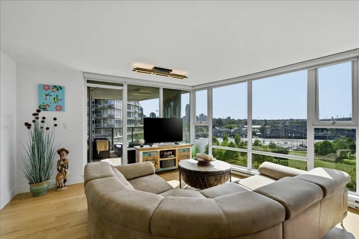 Bright living room with a beige sectional sofa, round coffee table, TV, and large windows with a city view.