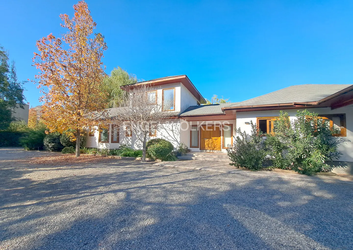 Two-story white house with brown trim, a gray roof, and a gravel driveway on a sunny day.