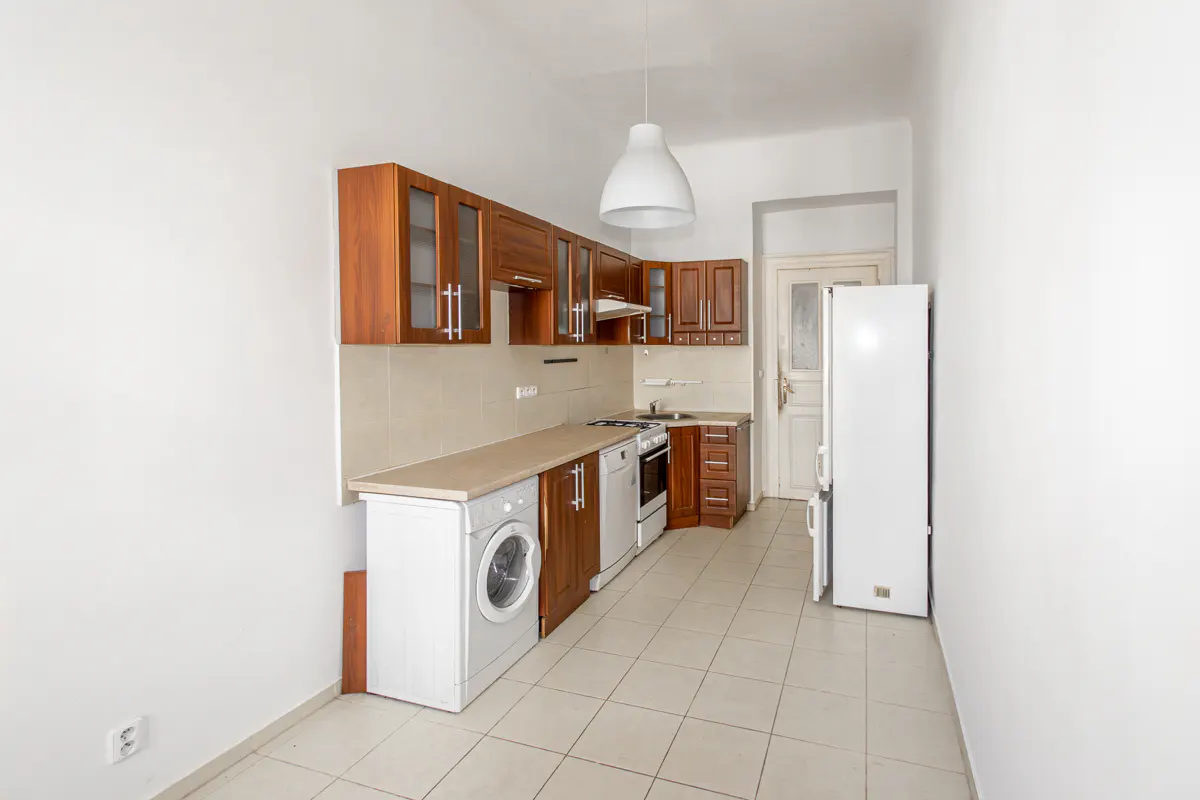 A bright kitchen with brown cabinets, white appliances, and beige tile flooring. A white pendant light hangs from the ceiling.