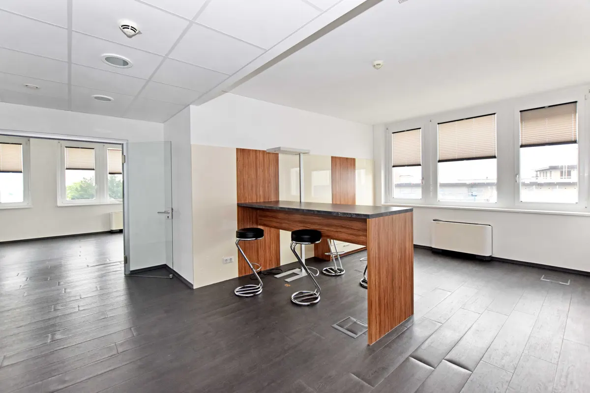 Bright office space with dark wood floors, a breakfast bar with stools, and large windows with blinds.