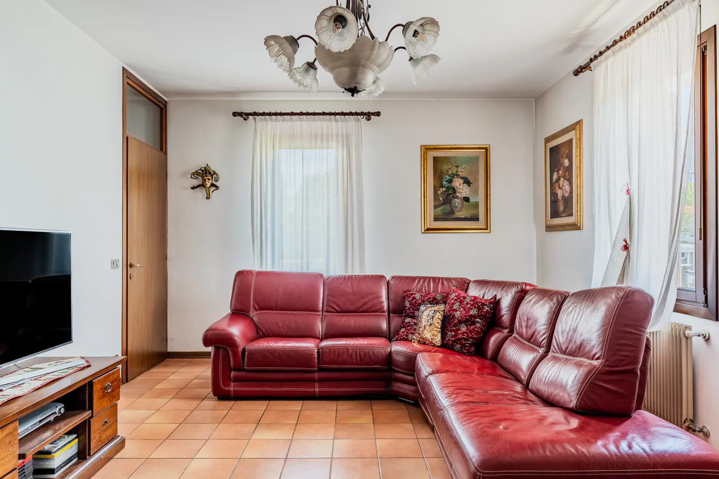 Living room with a red leather sectional sofa, tile floor, paintings, and a chandelier.