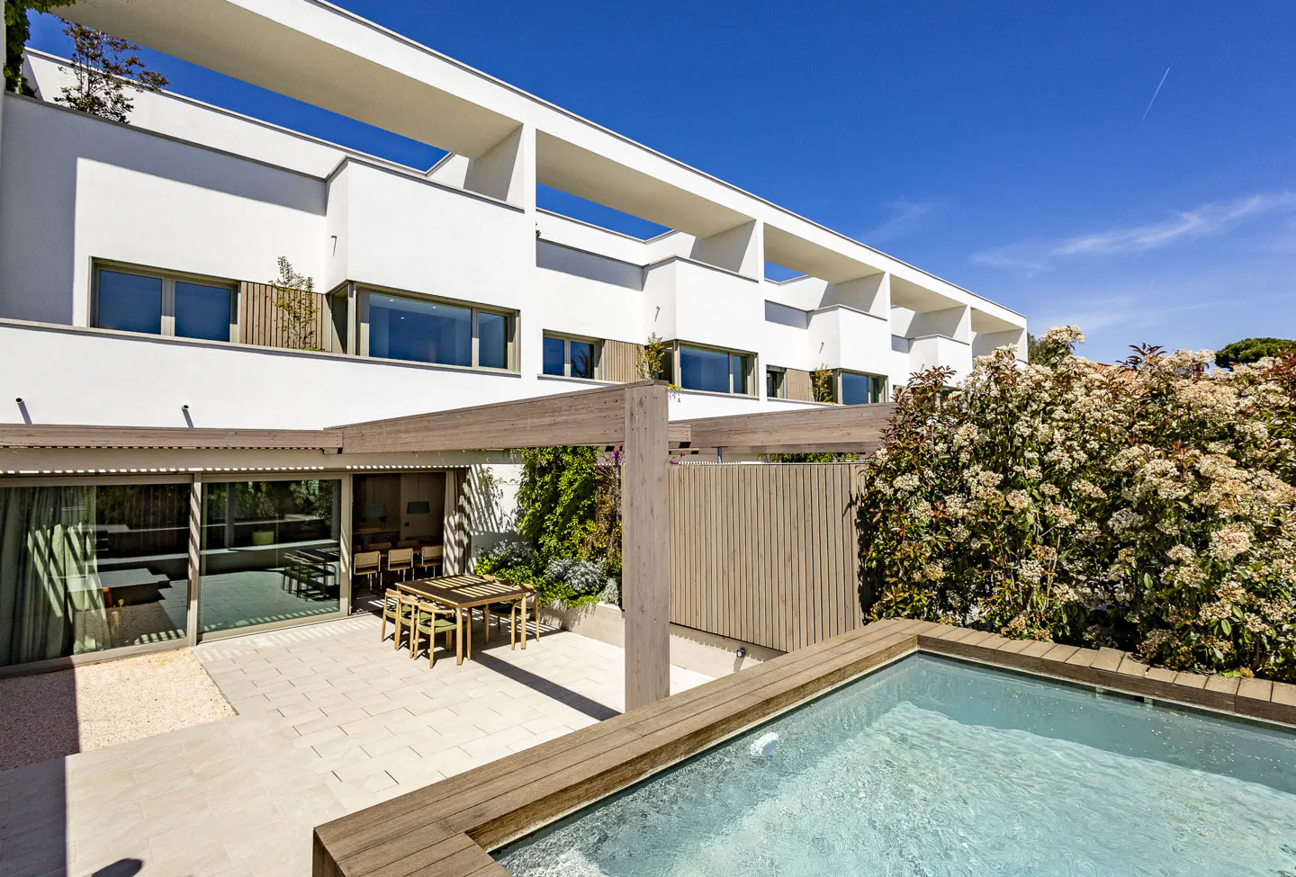 Modern white house with a pool, patio, and outdoor dining area under a blue sky.