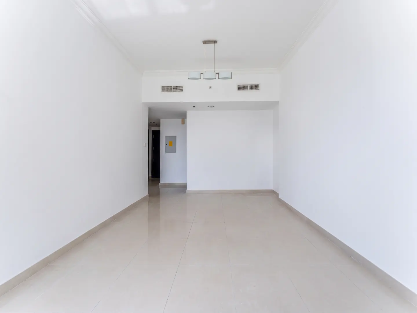 Empty room with white walls, beige tile floor, and a modern chandelier. A doorway leads to another room.