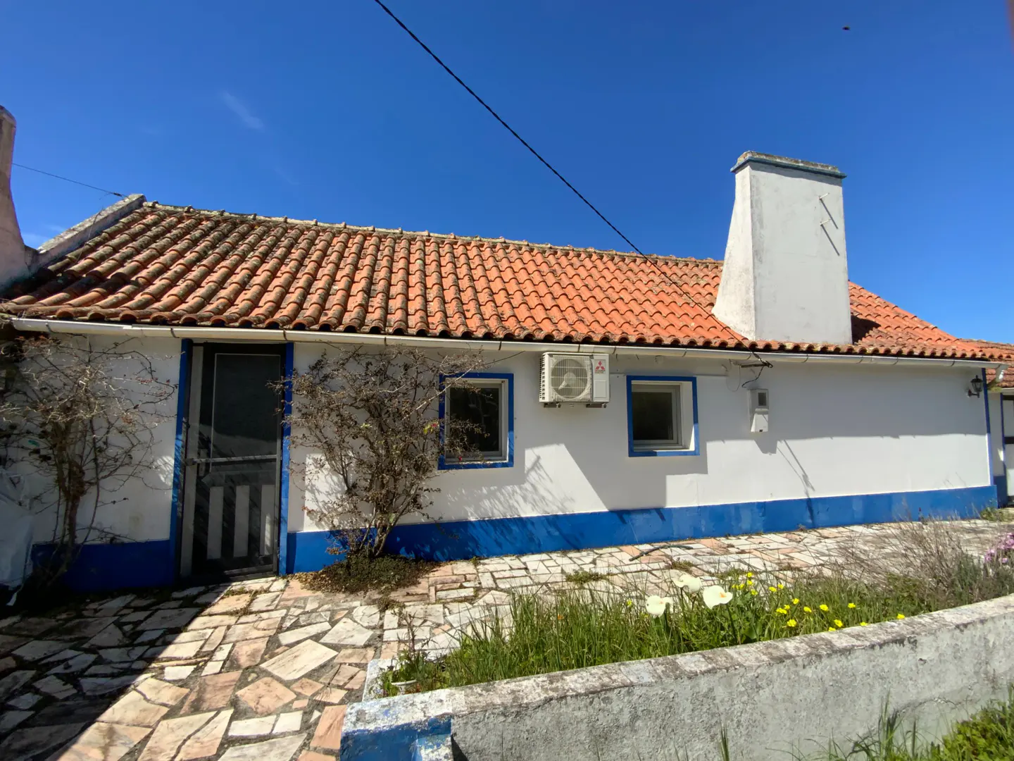 Exterior view of a white house with a blue trim, red tile roof, and stone walkway under a clear blue sky.