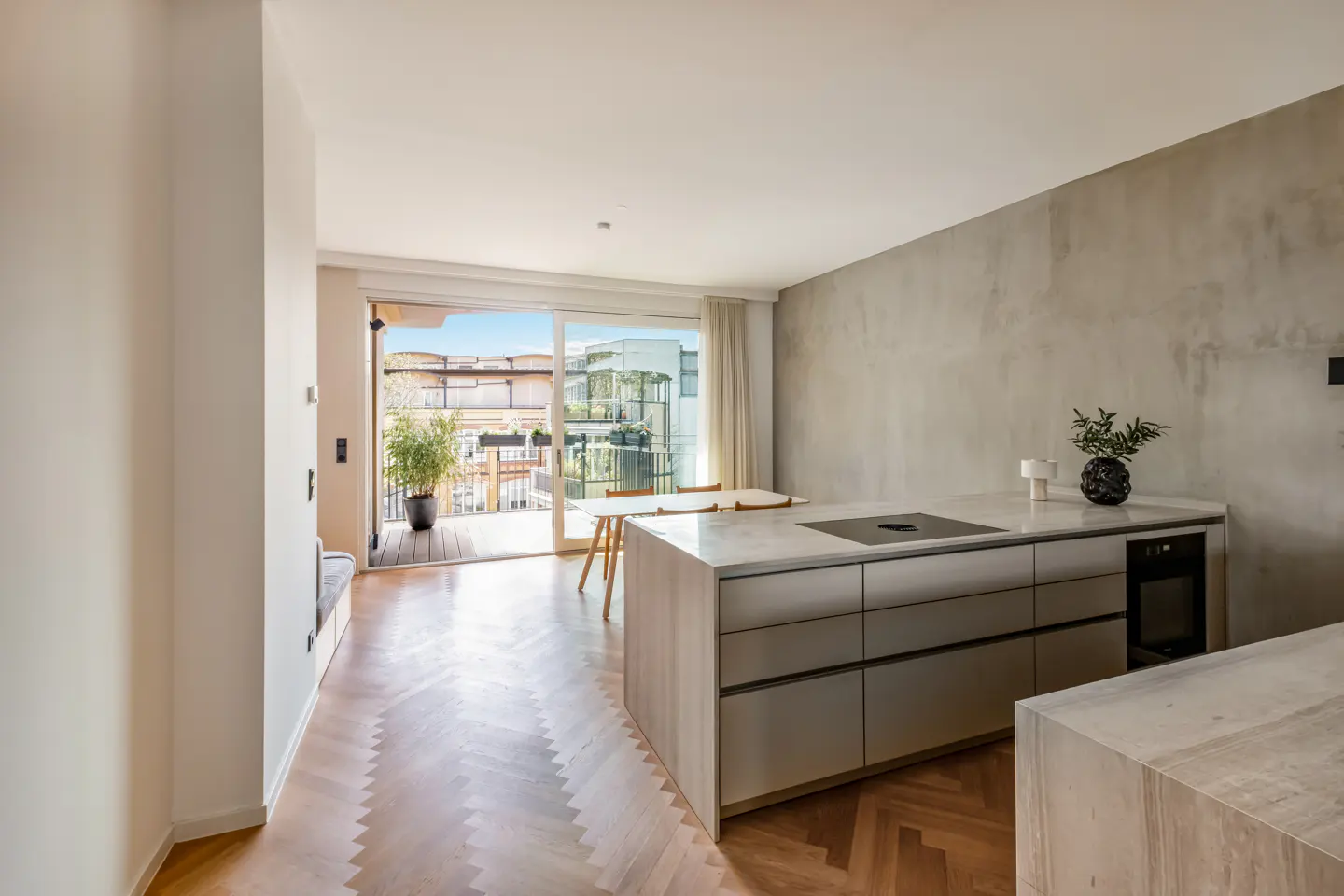 Bright, modern kitchen with herringbone wood floors, a gray island, and sliding glass doors to a balcony with a potted plant.