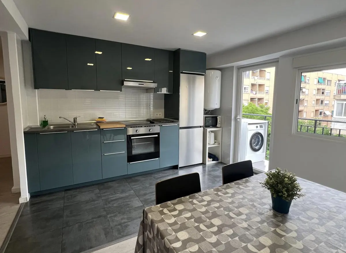 Modern kitchen with dark blue cabinets, stainless steel appliances, and a dining table with a patterned tablecloth.