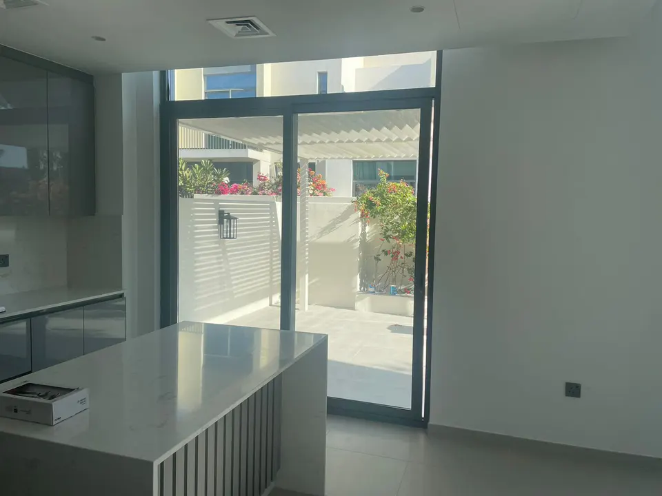Modern kitchen with a white marble island, dark cabinets, and large sliding glass doors opening to a sunny patio garden.