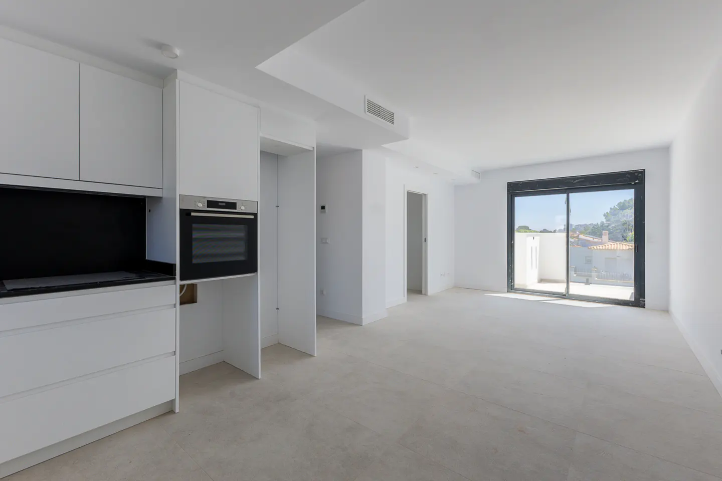 Modern minimalist kitchen with white cabinets, black backsplash, built-in oven, and sliding glass doors to a bright terrace.