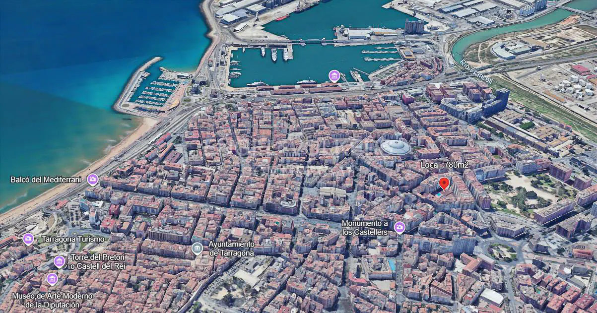Aerial view of Tarragona, Spain, showing dense urban buildings in shades of brown and red, near the blue Mediterranean Sea.
