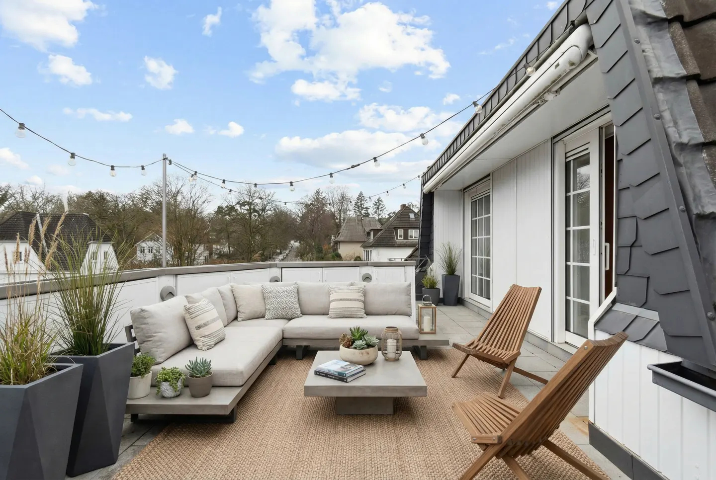 Rooftop patio with a beige sectional sofa, a square coffee table, and two wooden chairs on a jute rug. String lights overhead.