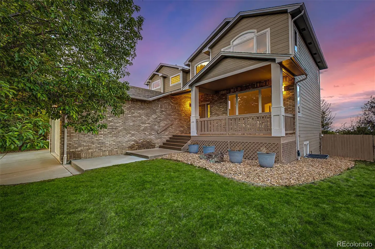 Two-story house with a brick and siding exterior, a front porch, and a green lawn at dusk.