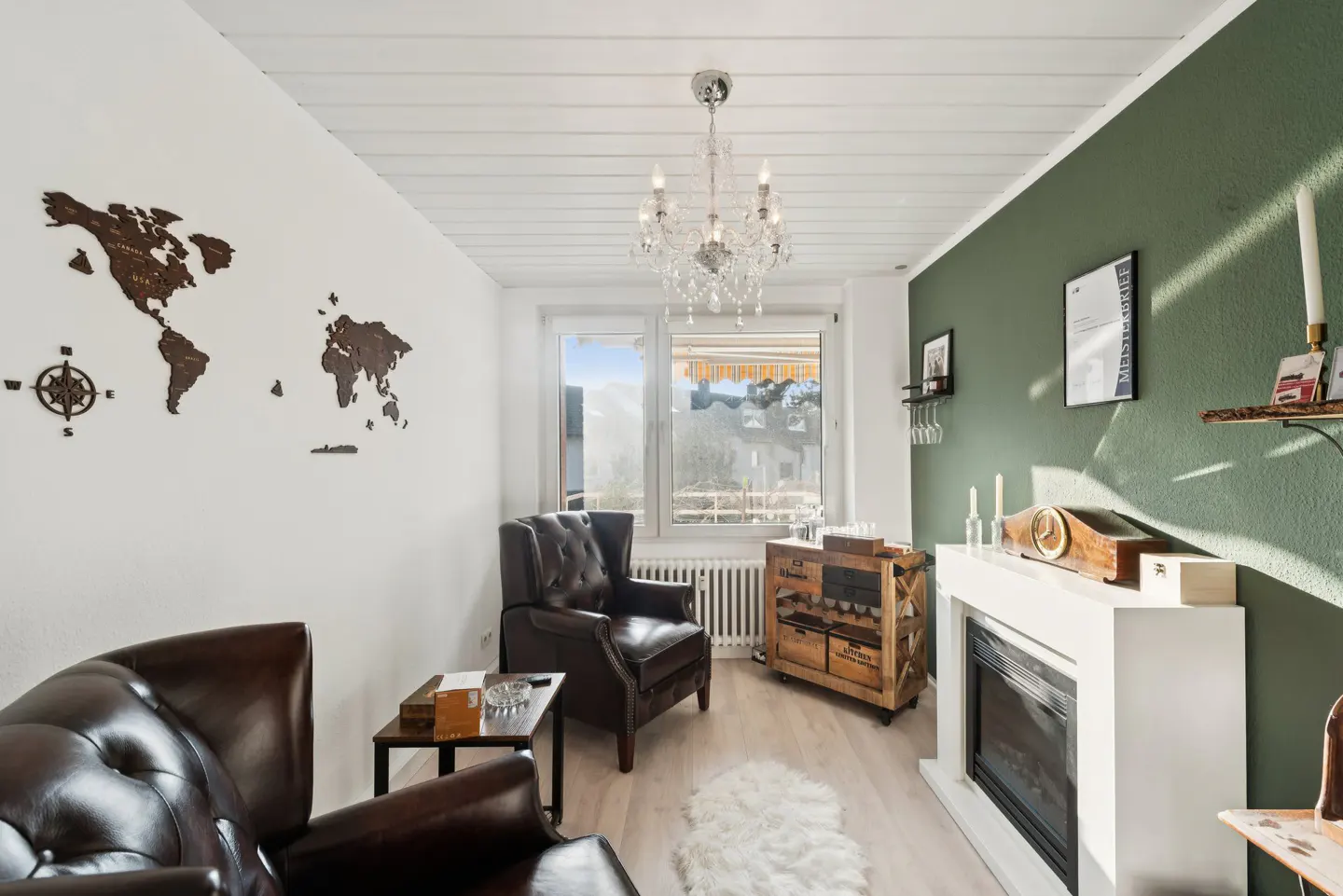 Living room with dark leather chairs, white walls with a wooden world map, and a green accent wall with a white fireplace.