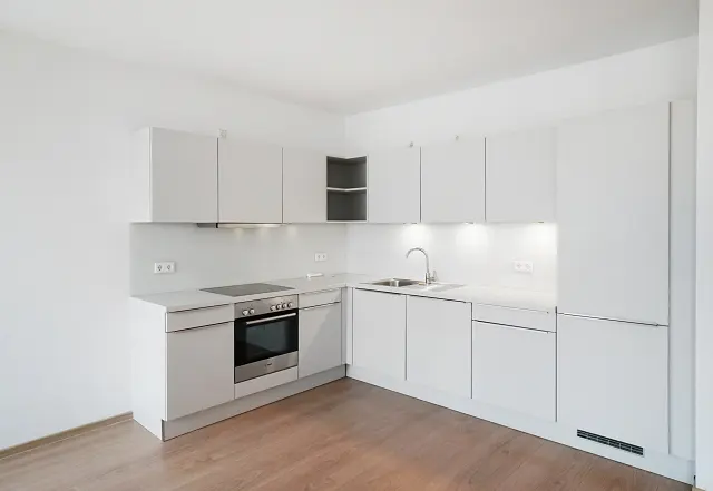 Bright, modern kitchen with white cabinets, countertops, and appliances. Wood flooring adds warmth to the minimalist design.