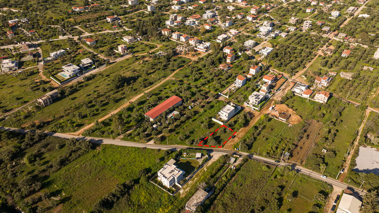 Aerial view of a vacant lot outlined in red, surrounded by green grass, trees, and houses in a rural area.