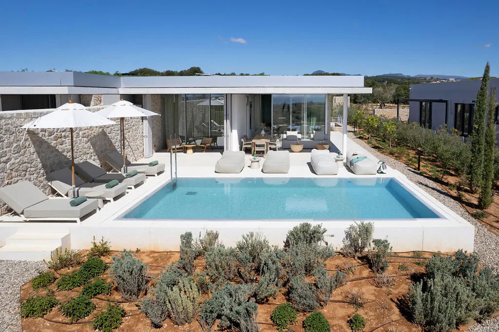 A modern villa with a pool, lounge chairs, and white umbrellas under a clear blue sky.
