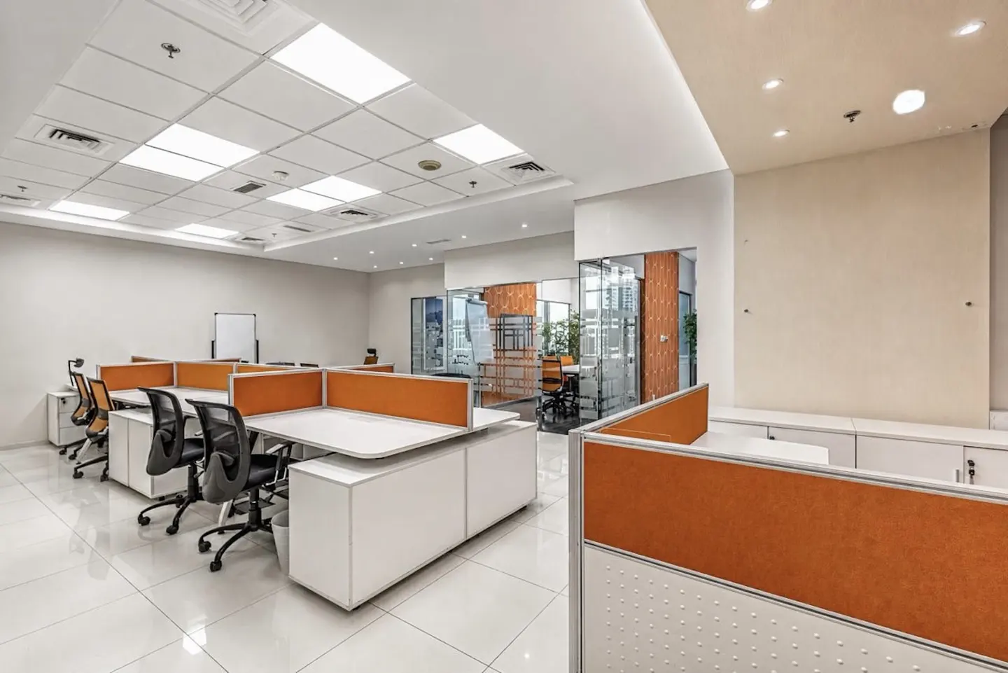 Bright, modern office space with white desks, orange partitions, and black chairs on a white tiled floor.