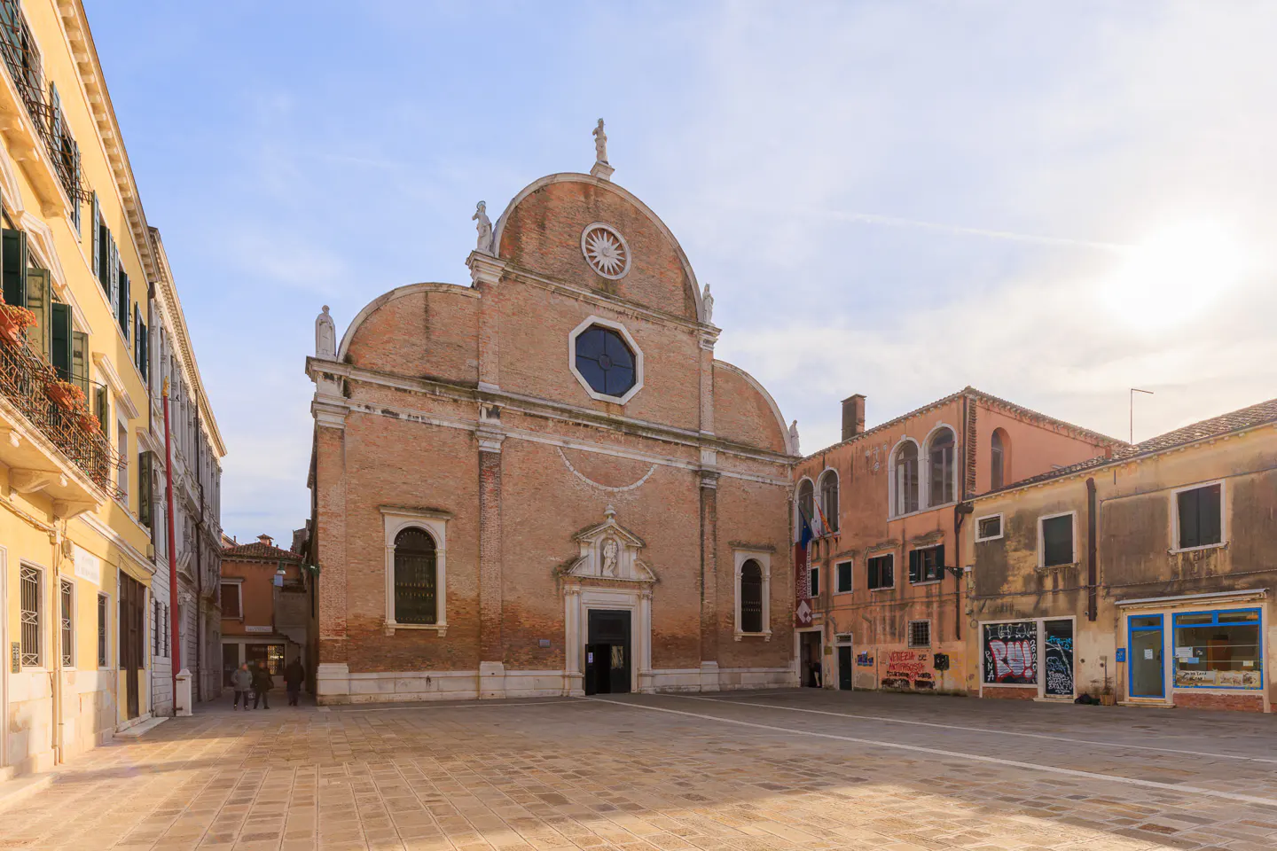 Venice, Italy: A brick church with a statue on top stands in a square with buildings on either side.