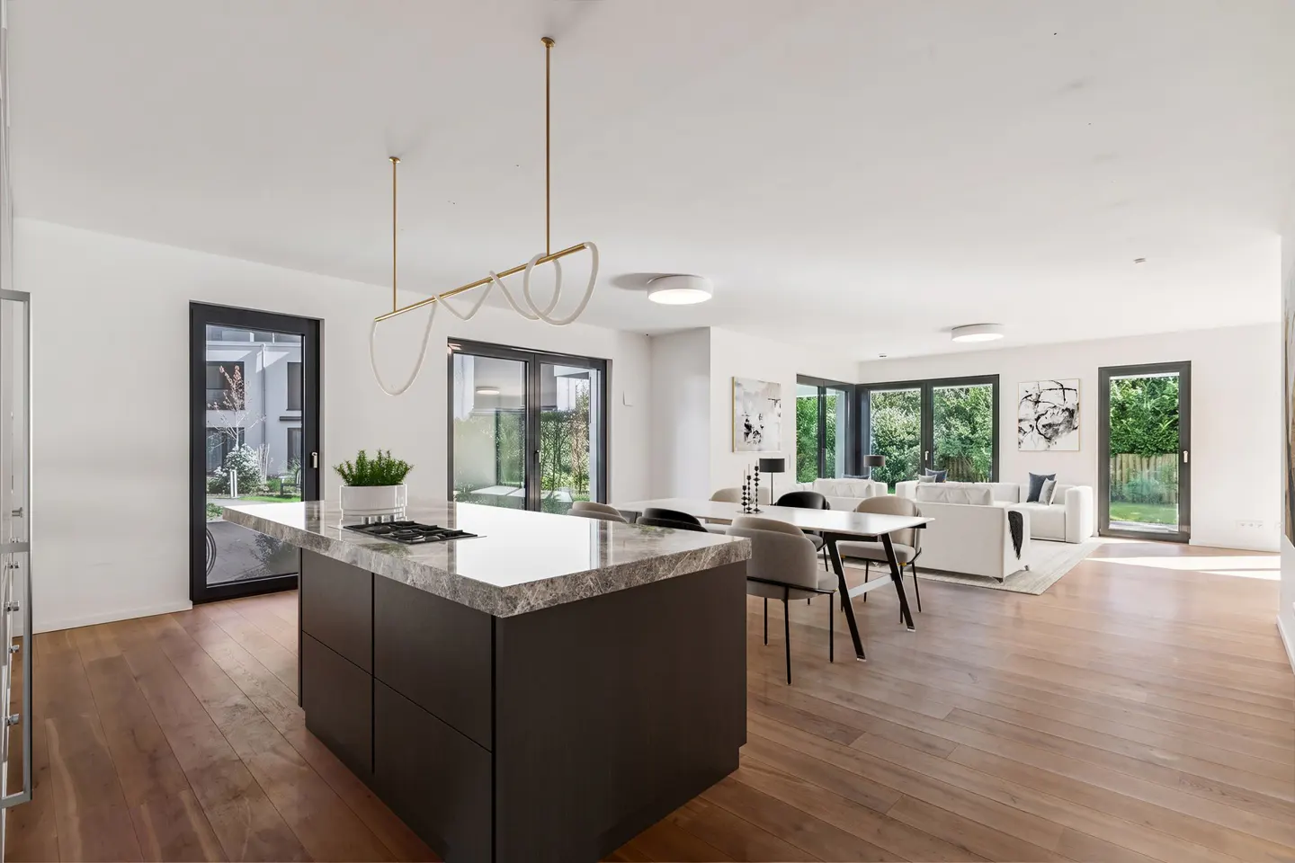 Open-concept living space with wood floors, a kitchen island with a marble countertop, and a dining table with gray chairs.