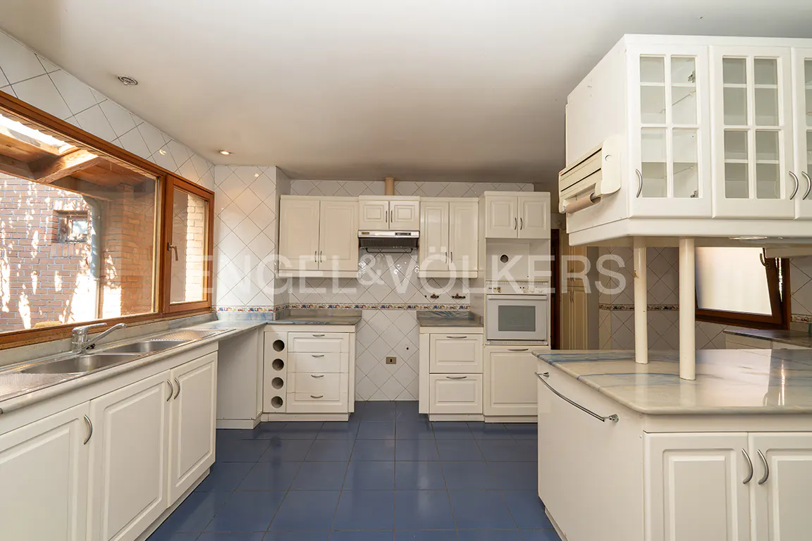 A bright kitchen with white cabinets, blue tile floor, and a large window.
