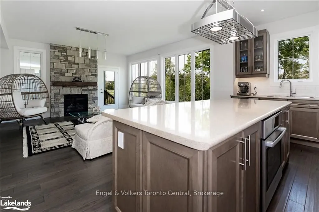 A modern kitchen and living room with dark wood floors, a stone fireplace, and egg chairs.