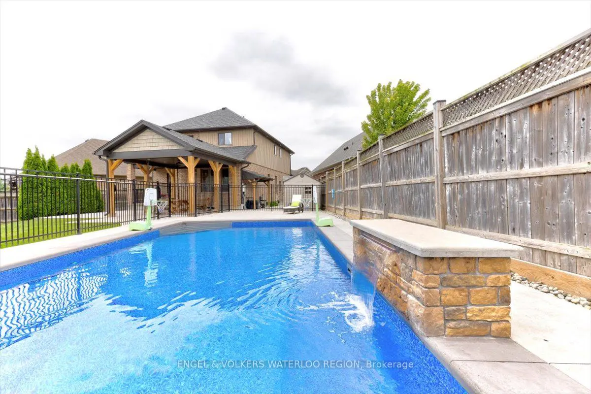 Backyard pool with blue water, stone waterfall feature, and wooden fence. A covered patio and house are in the background.