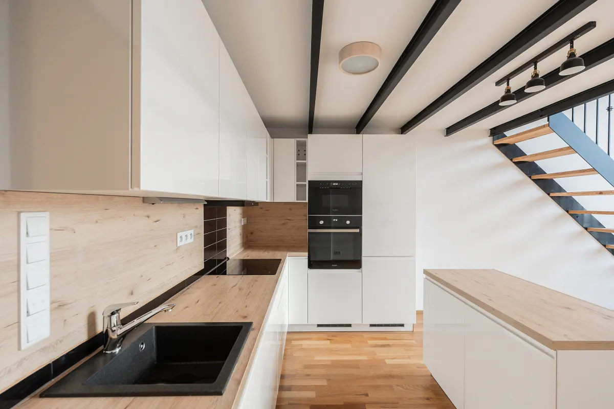 Bright kitchen with white cabinets, wood countertops, and black sink. Stairs with black railing are visible in the background.