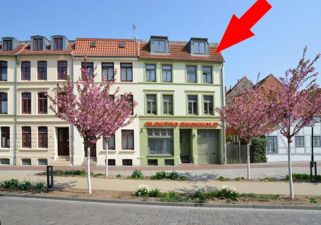 Row of townhouses with pink trees in front. A red arrow points to the top floor of the middle building.