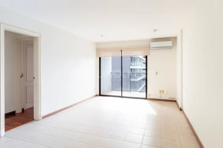 Bright, empty room with white walls, tile floor, and a sliding glass door to a balcony. A doorway is visible on the left.