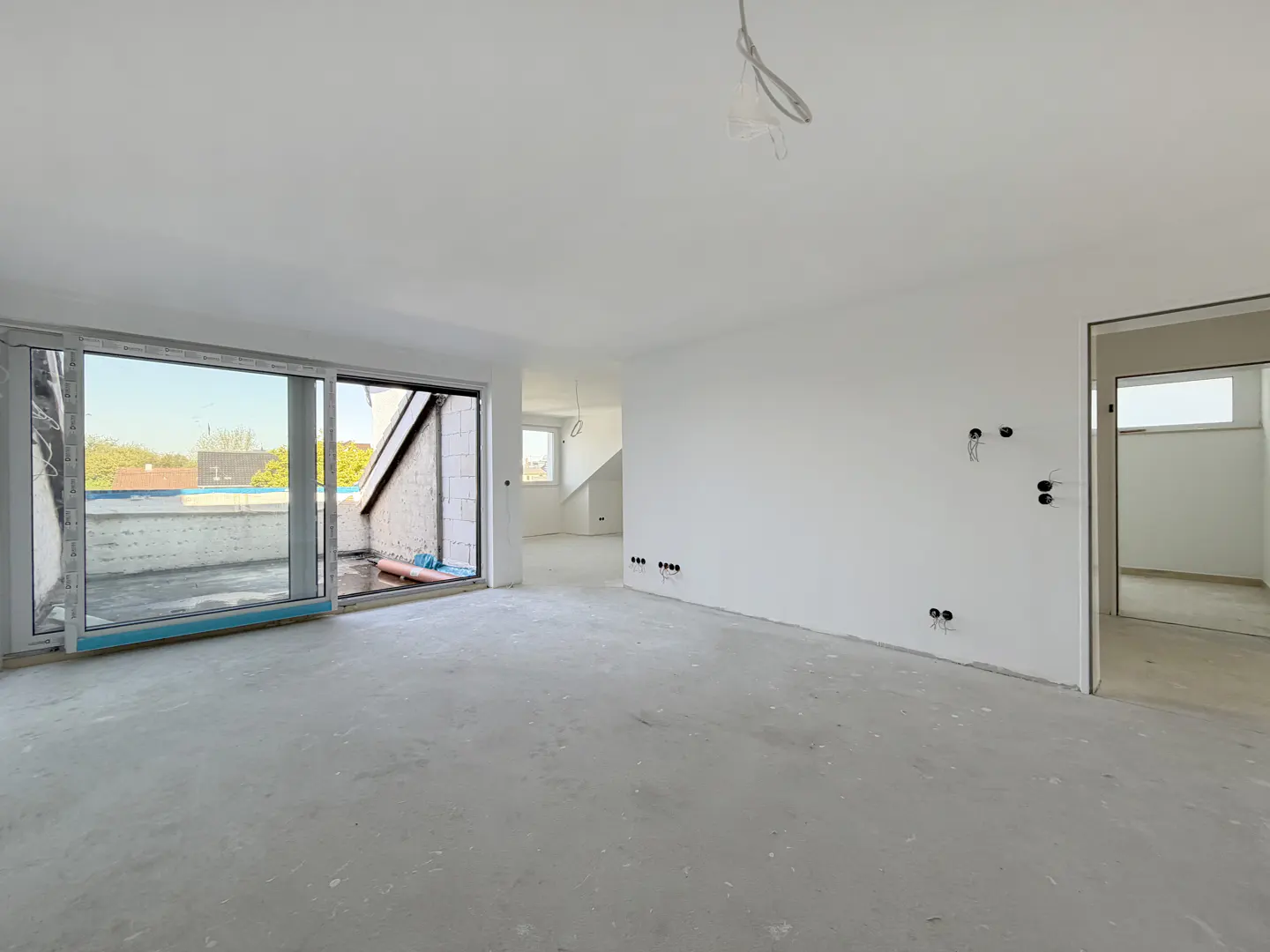 Unfinished room with white walls, a concrete floor, and a large sliding glass door to a balcony. Electrical outlets are visible.