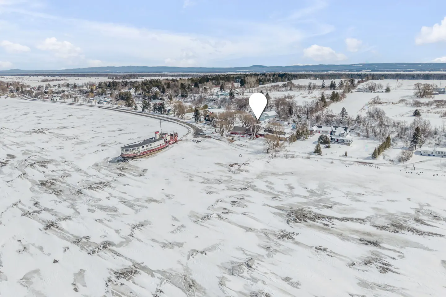 Aerial view of a snow-covered landscape with a red and white boat near a road, and a white location pin.