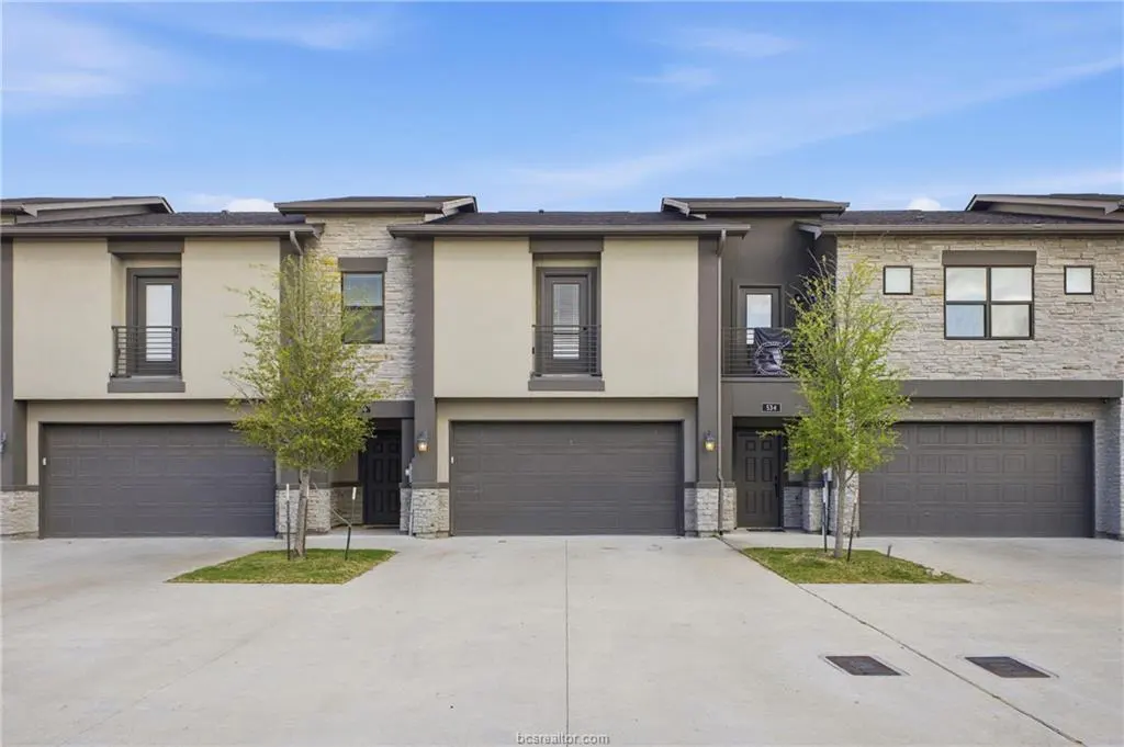 Three modern townhouses with gray garages and stone accents under a blue sky.