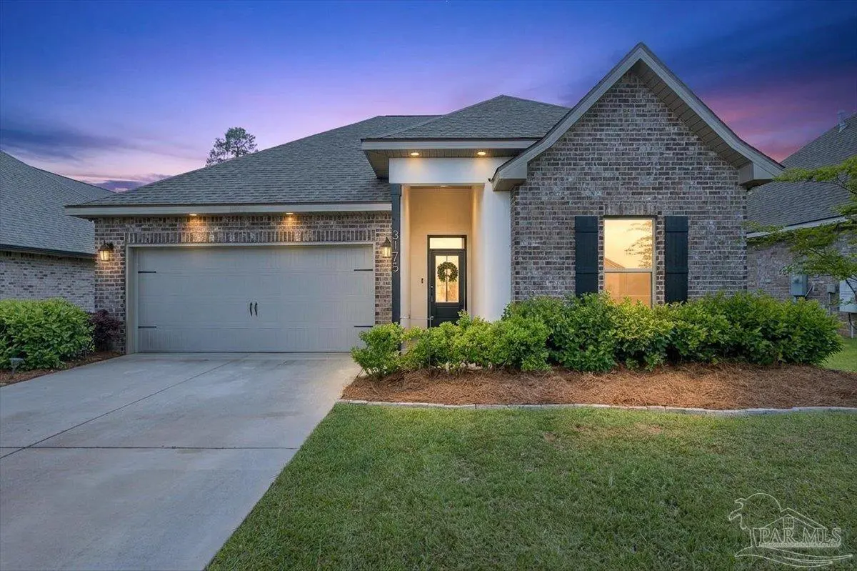 A single-story brick house with a gray roof, a two-car garage, and a green lawn at dusk.