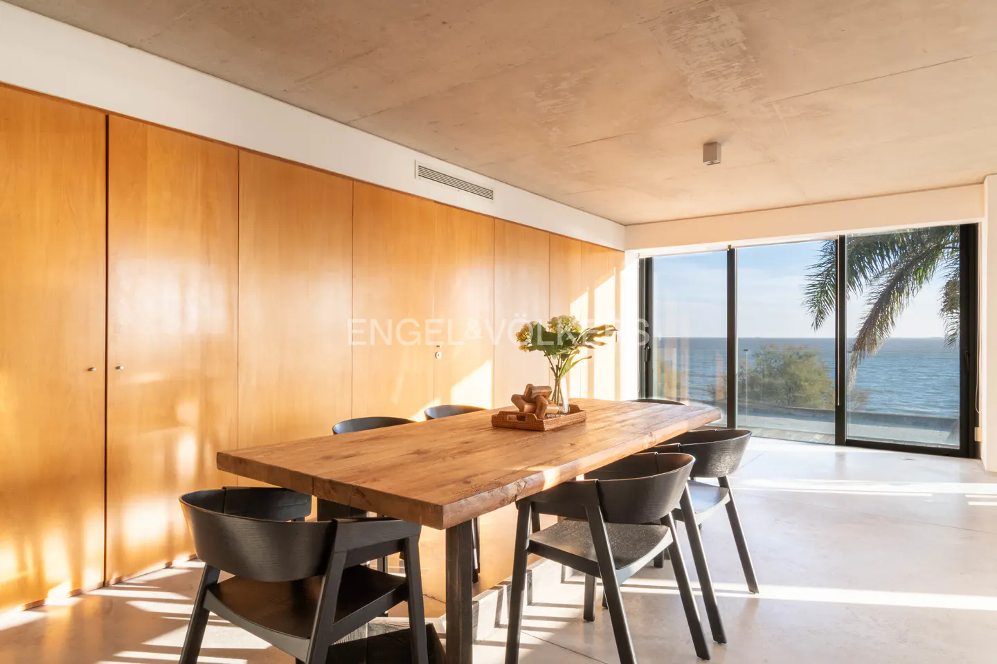 Dining room with a wooden table, black chairs, and a view of the ocean through large windows.