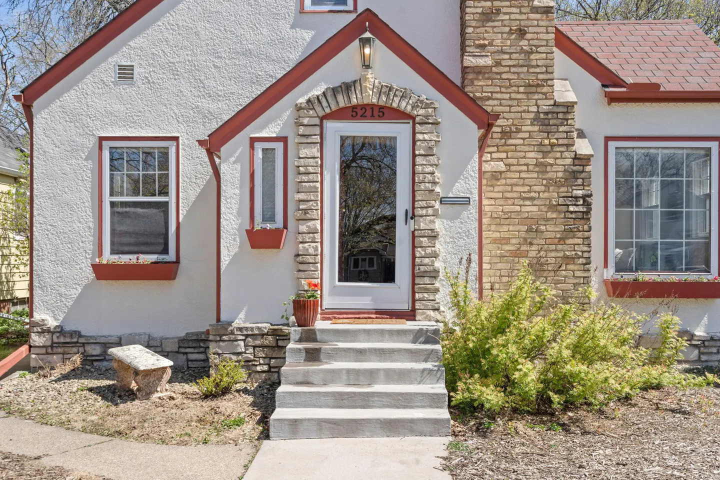 Exterior of a white stucco house with red trim, a brick chimney, and a stone-framed front door with the address 5215 above it.