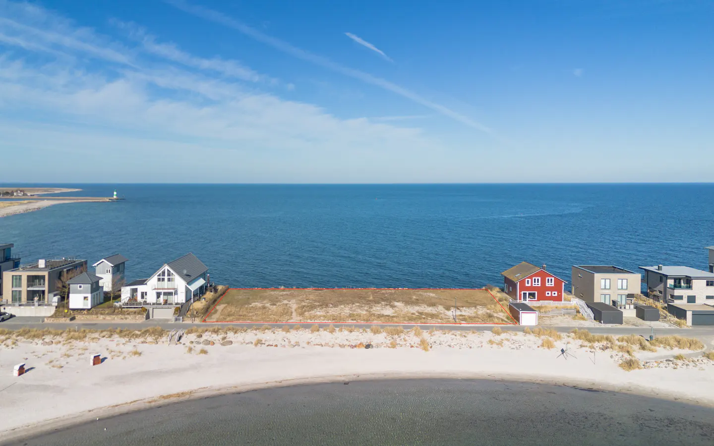 Waterfront property with a vacant lot outlined in red, sandy beach, and blue sky. Houses are on either side of the lot.
