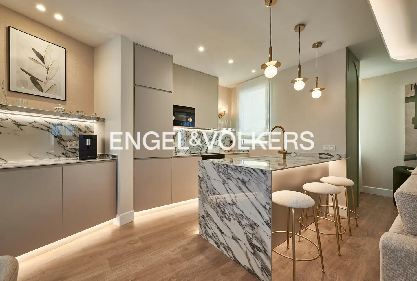 Modern kitchen with beige cabinets, marble island, three gold pendant lights, and wood flooring.